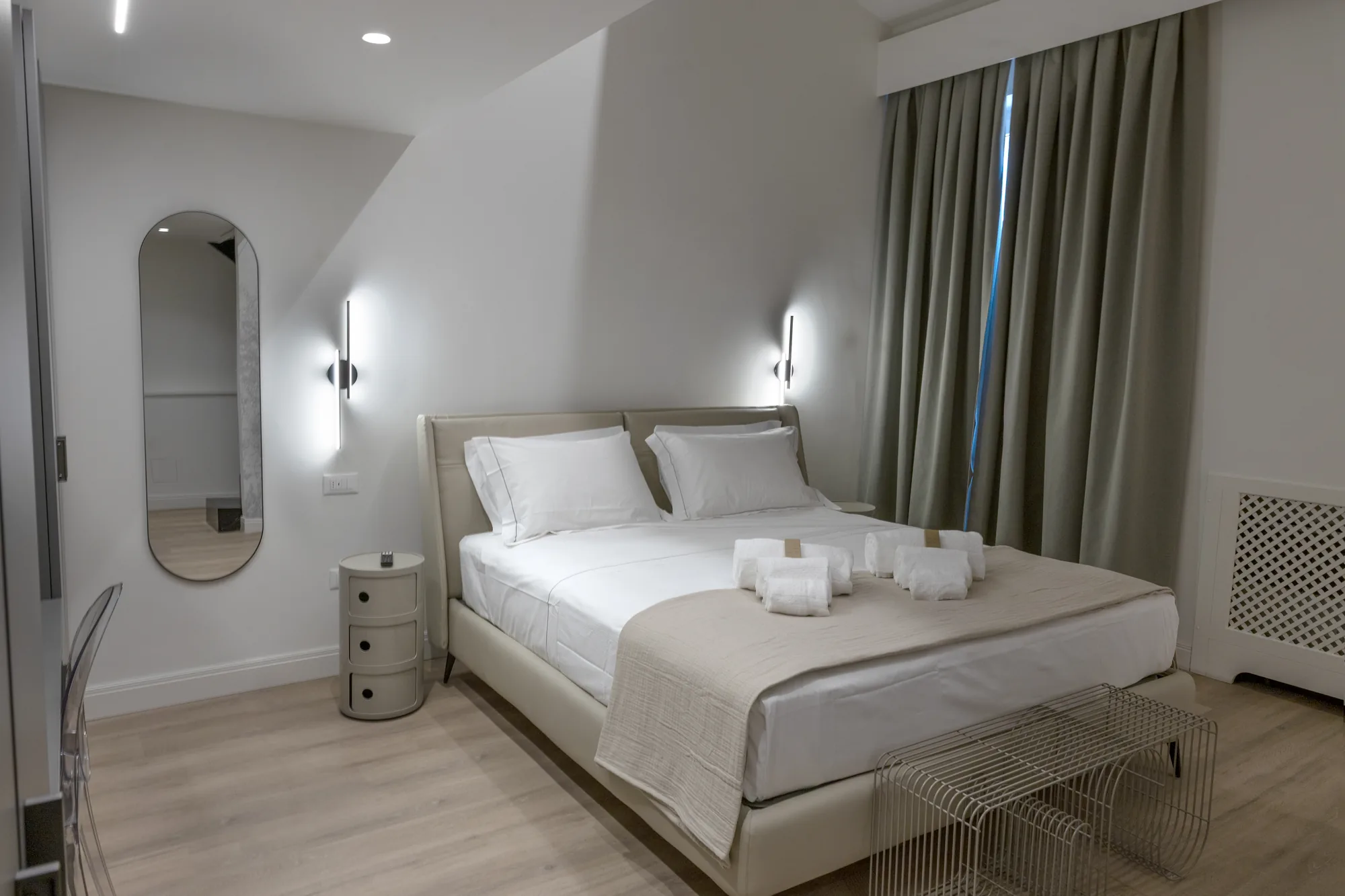 Modern bedroom with a double bed, nightstands, wall mirror, and dark curtains