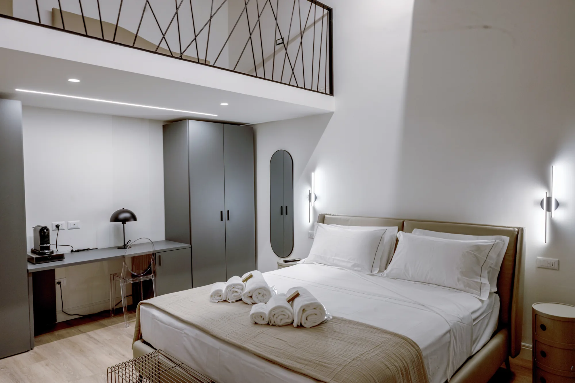Modern bedroom with a double bed, desk, wardrobe, and folded towels on the bed
