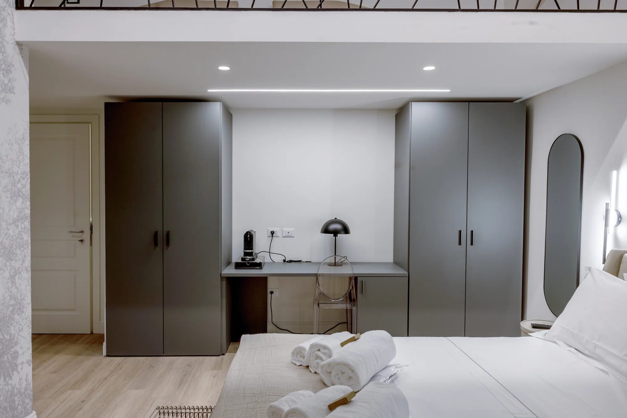 Modern bedroom with desk, gray wardrobes, and bed with folded towels
