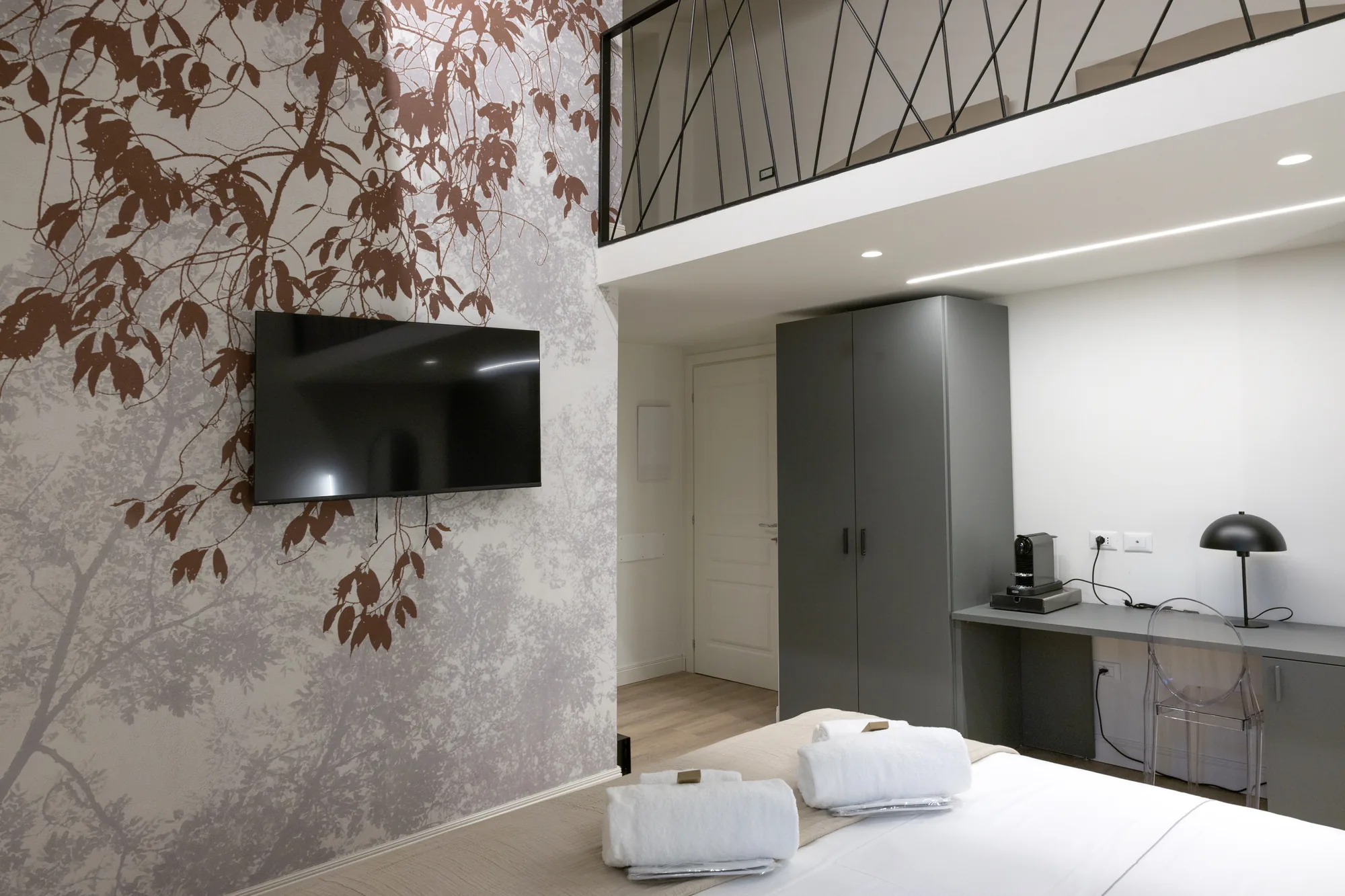Modern bedroom with wall-mounted TV, gray wardrobe, desk, and wall decorated with leaves