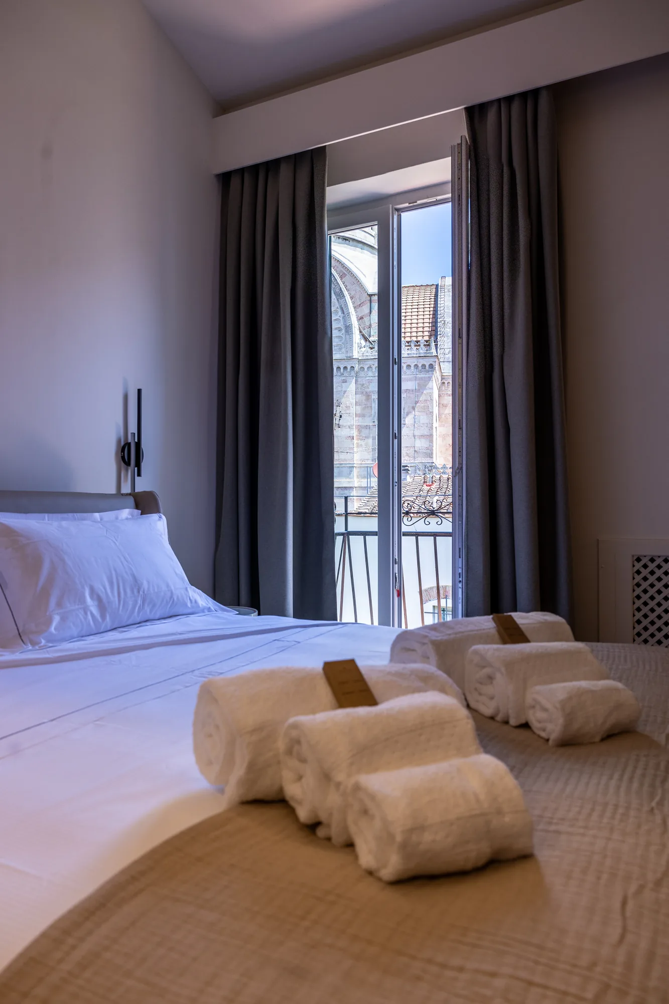 Hotel room with made bed, folded towels, and view of a historic building from the balcony