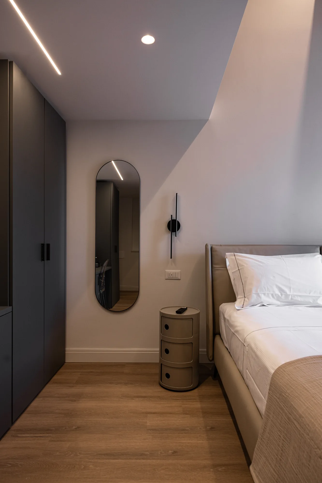Modern bedroom with bed, wardrobe, wall mirror, and cylindrical bedside table