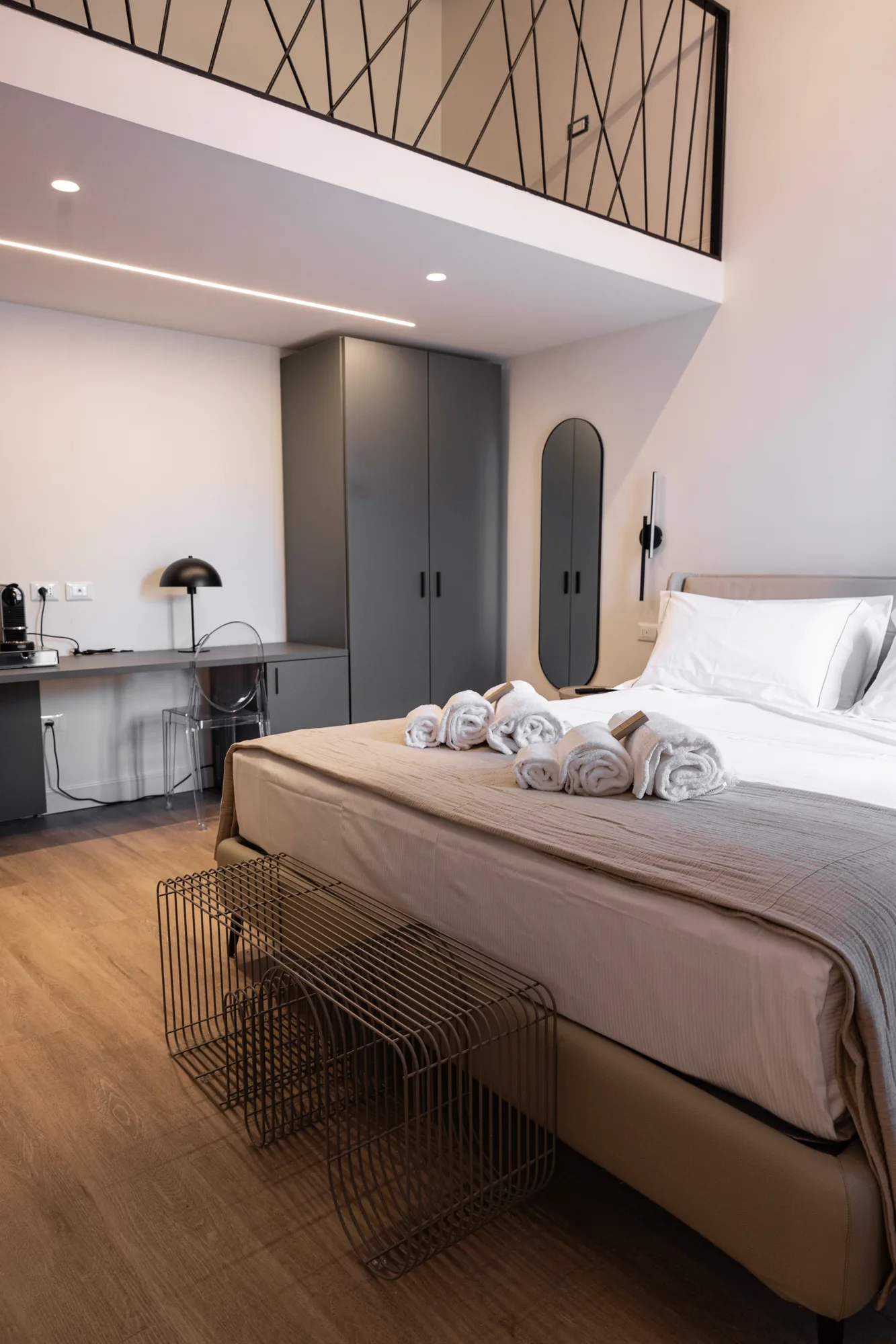 Modern bedroom with double bed, desk, gray wardrobe, and loft with black railing