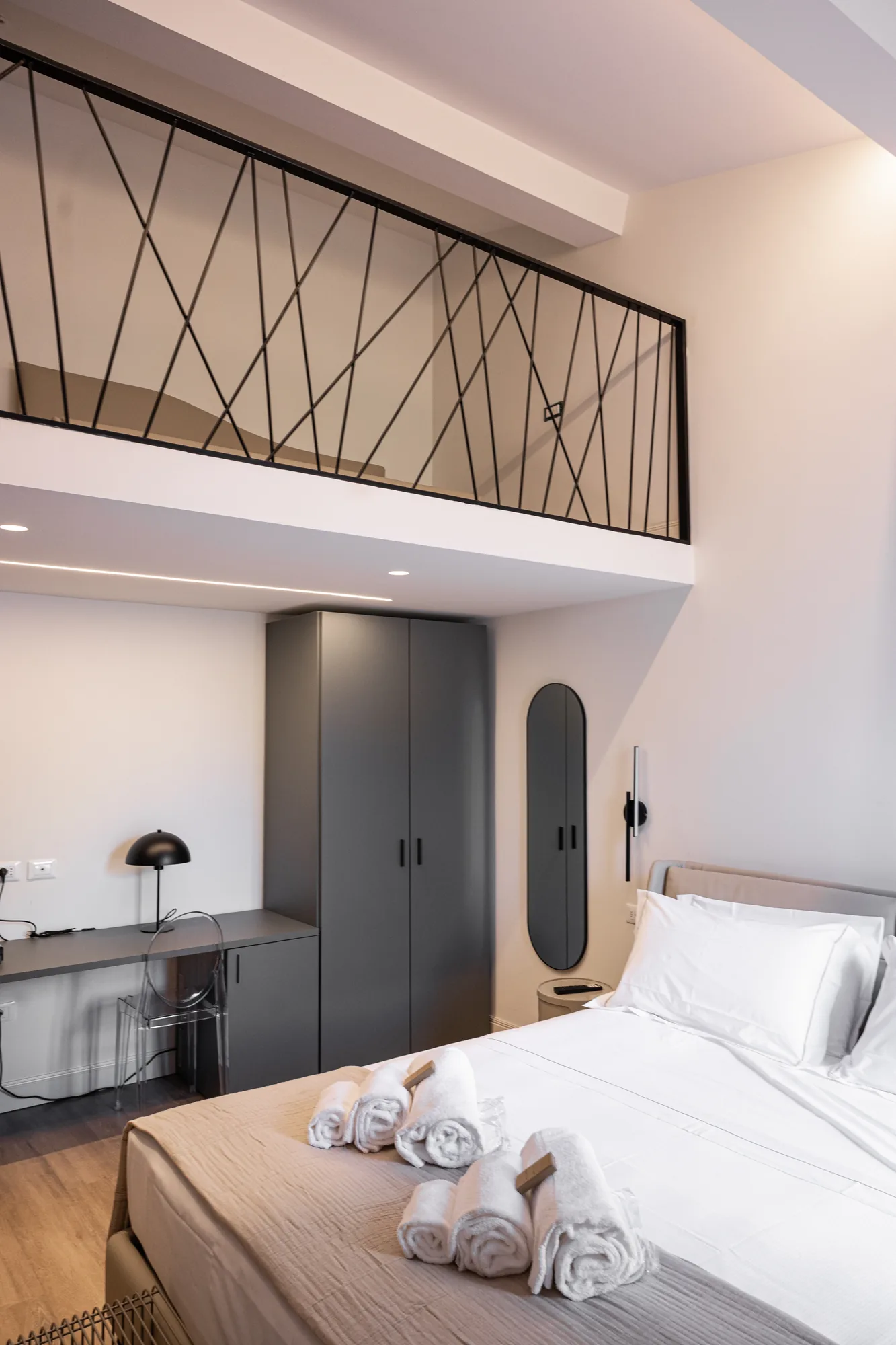 Modern bedroom with double bed, desk, wardrobe, and loft with black railing