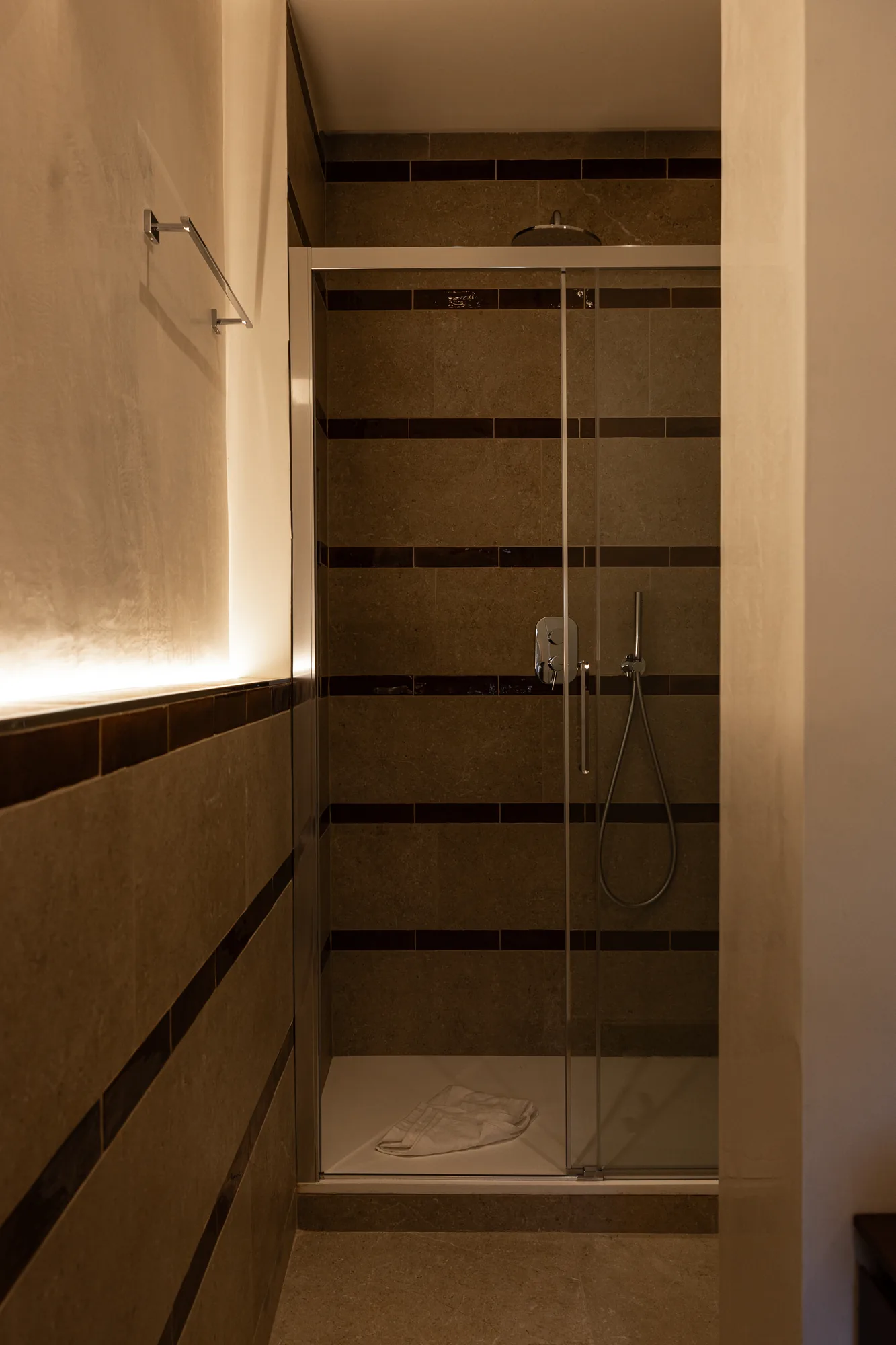 Modern shower with brown tiled walls and transparent glass enclosure