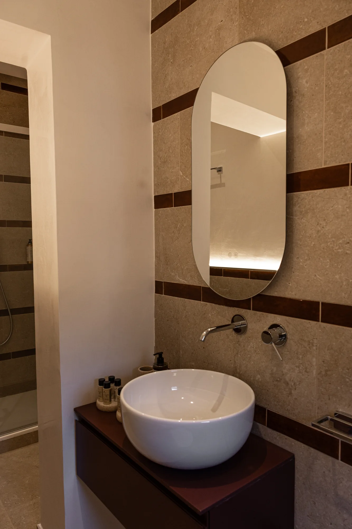 Modern bathroom with countertop sink, oval mirror, and stone walls