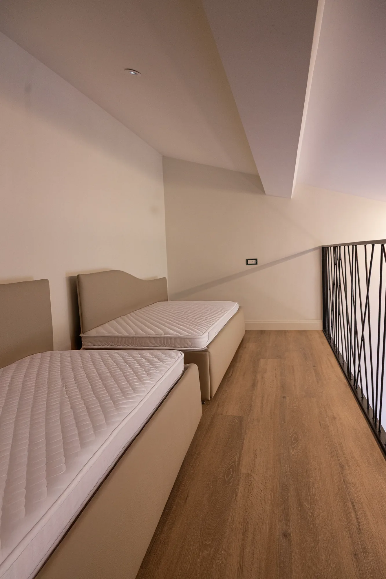 Attic bedroom with two single beds and wooden flooring, view from the upper floor