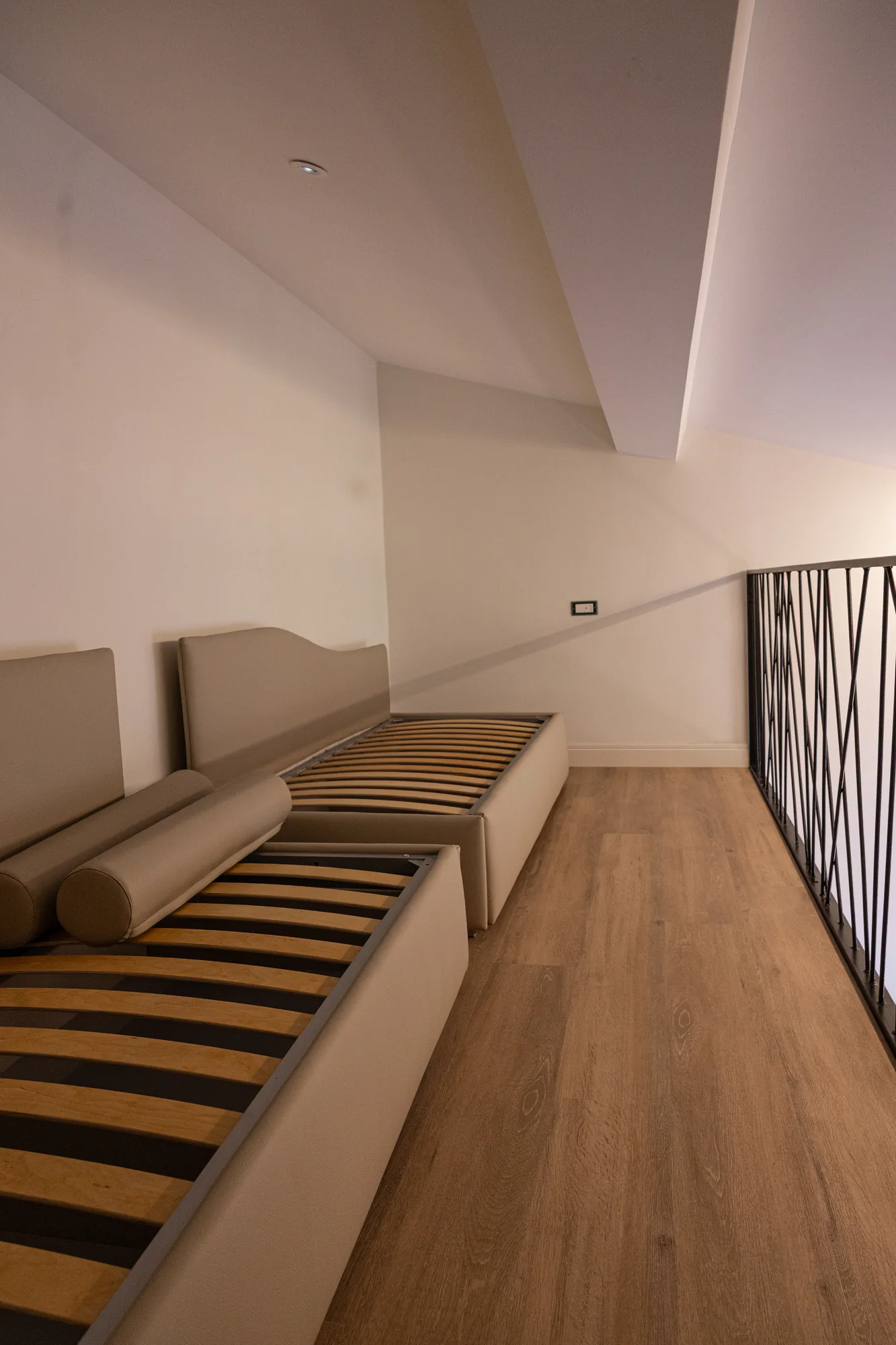Modern bedroom with two single beds and wooden floor, view of a loft with railing
