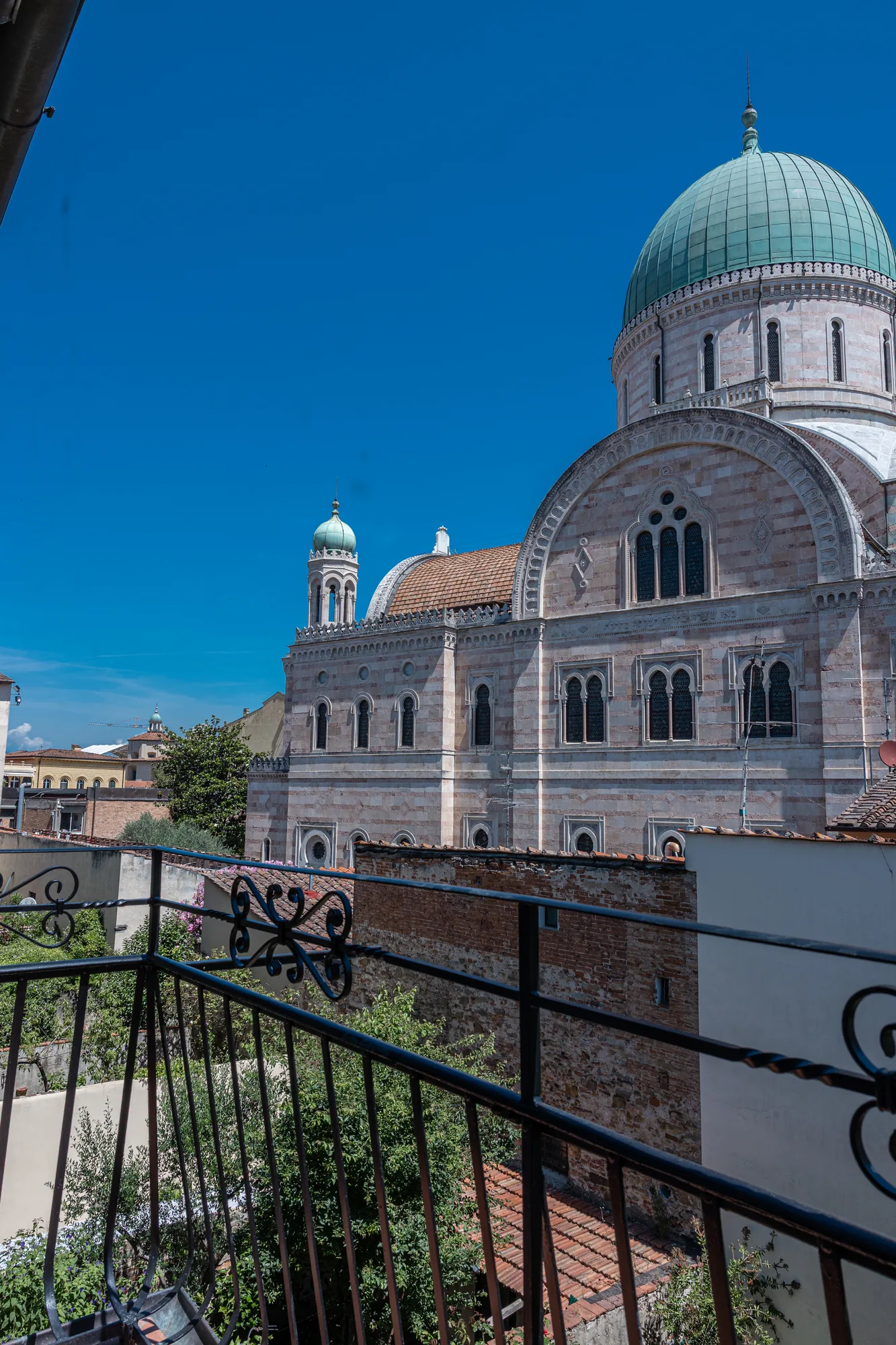 View of a large basilica with a green dome and bell tower, taken from a balcony under a clear sky