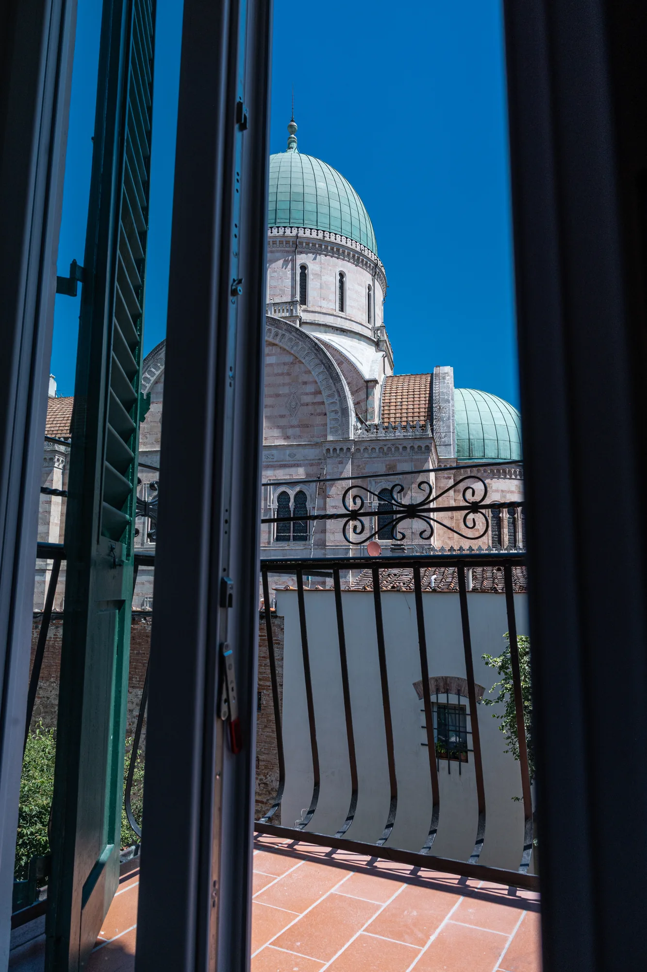 Dome of a basilica seen from a window with open shutters and a balcony in the foreground