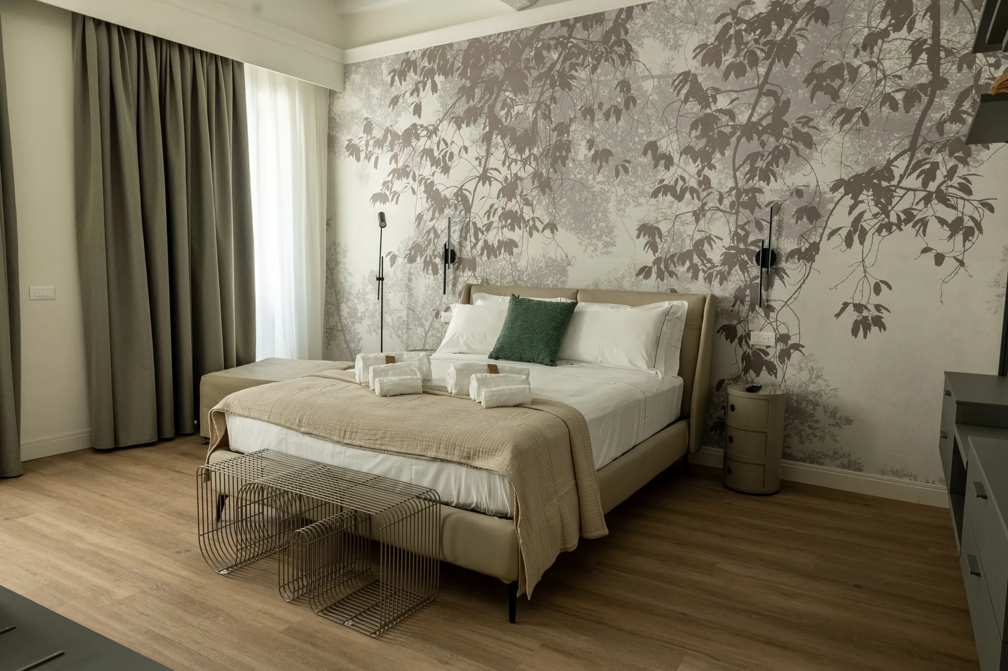 Camera da letto moderna con letto rifatto, parete decorata a motivi vegetali e tende scure