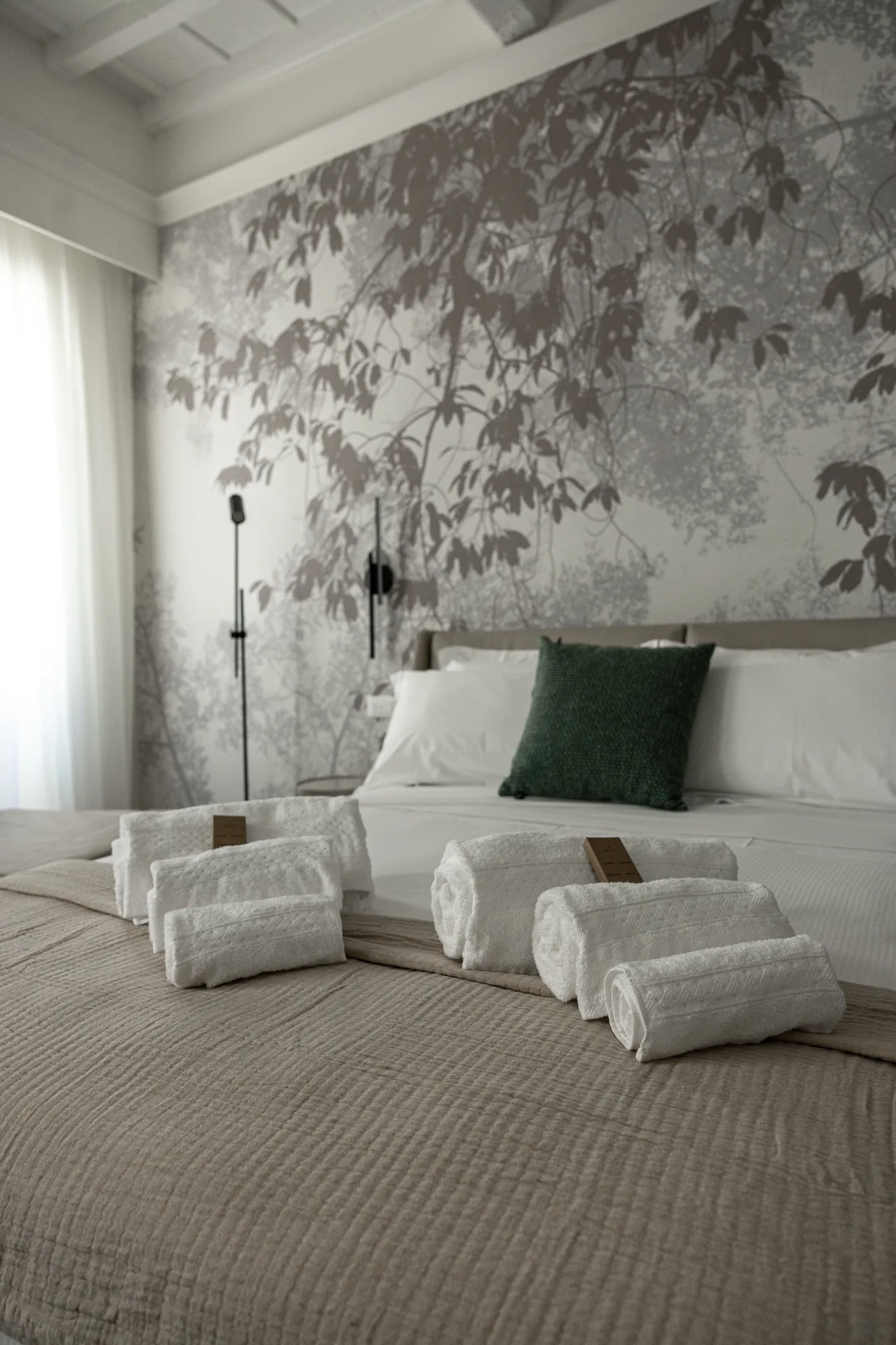 Camera da letto elegante con letto rifatto, asciugamani piegati e parete decorata con motivo di foglie