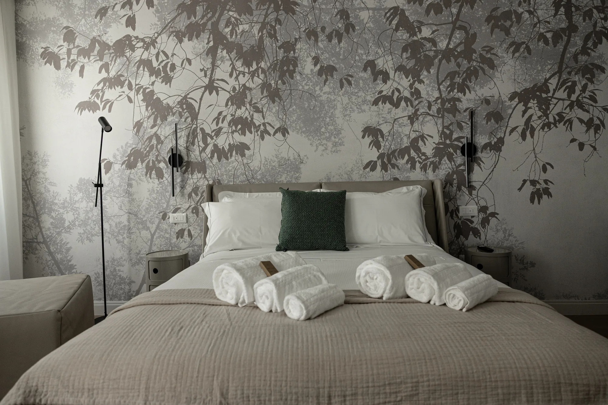 Camera da letto elegante con letto rifatto, asciugamani arrotolati e carta da parati con rami e foglie
