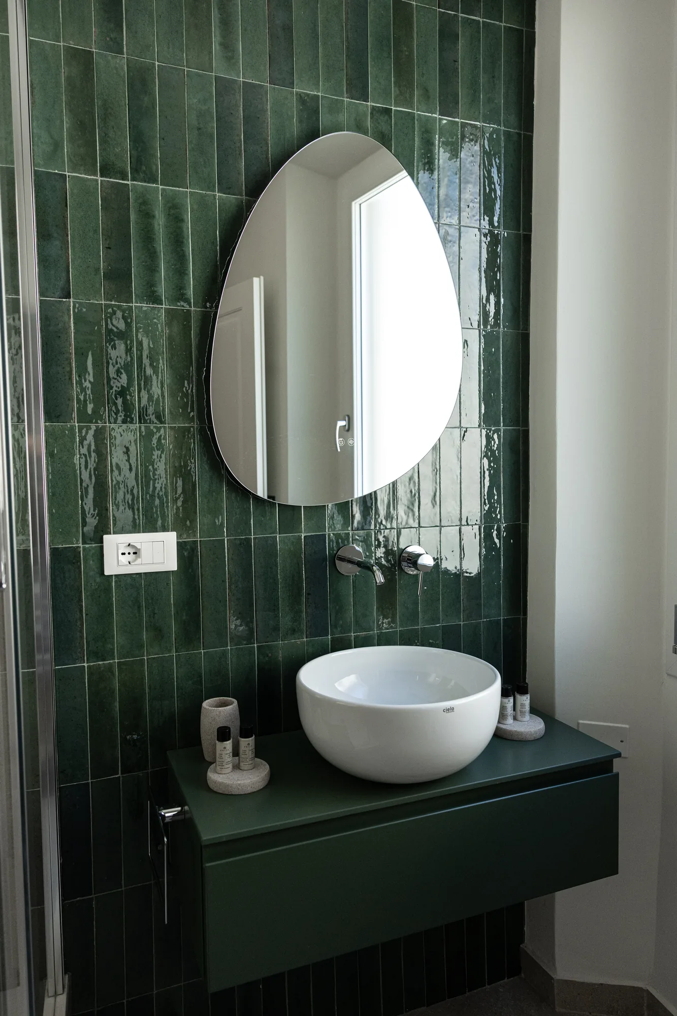 Lavabo da bagno moderno con specchio irregolare e piastrelle verdi lucide