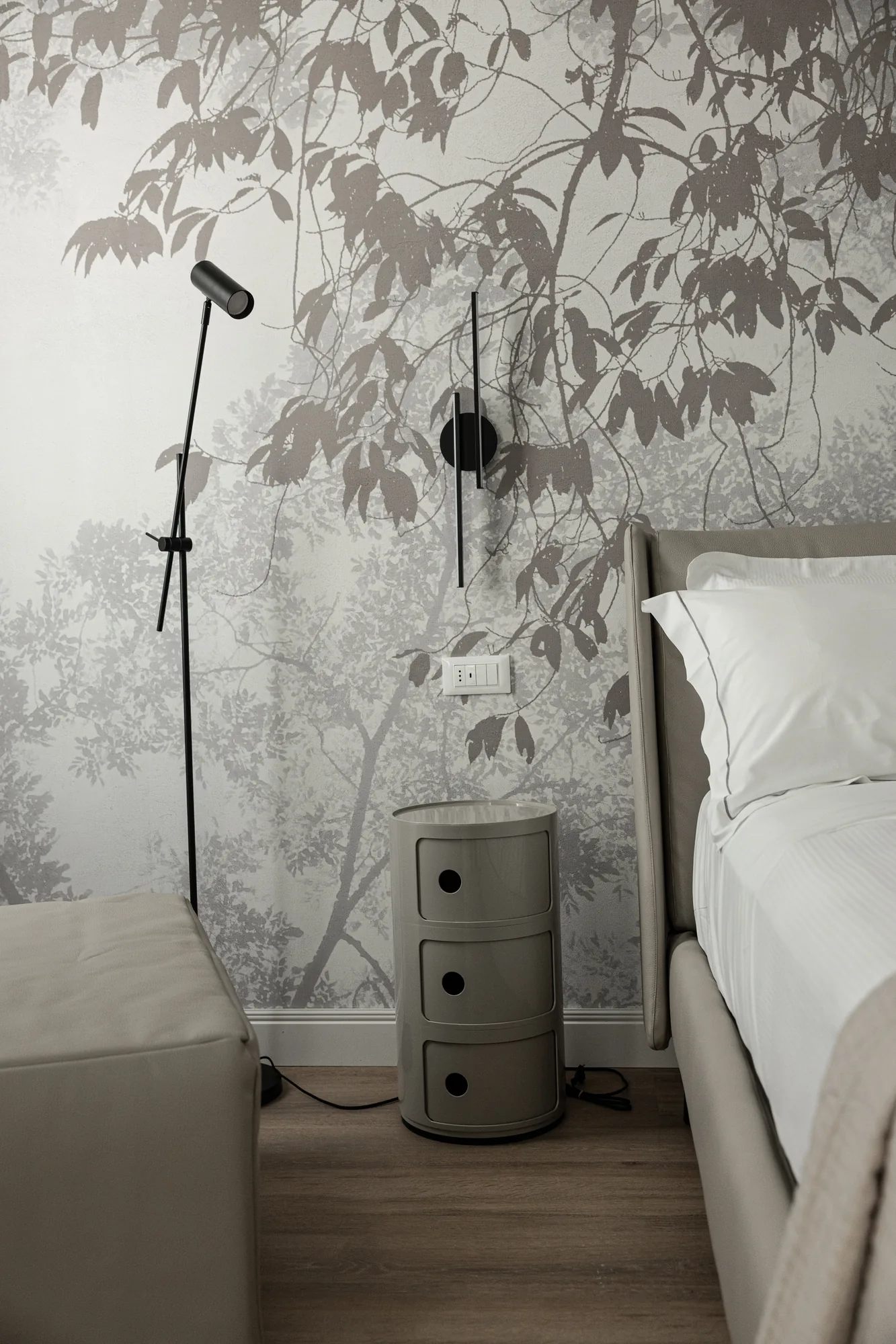 Camera da letto moderna con carta da parati a motivo di foglie, lampada da lettura e comodino accanto al letto