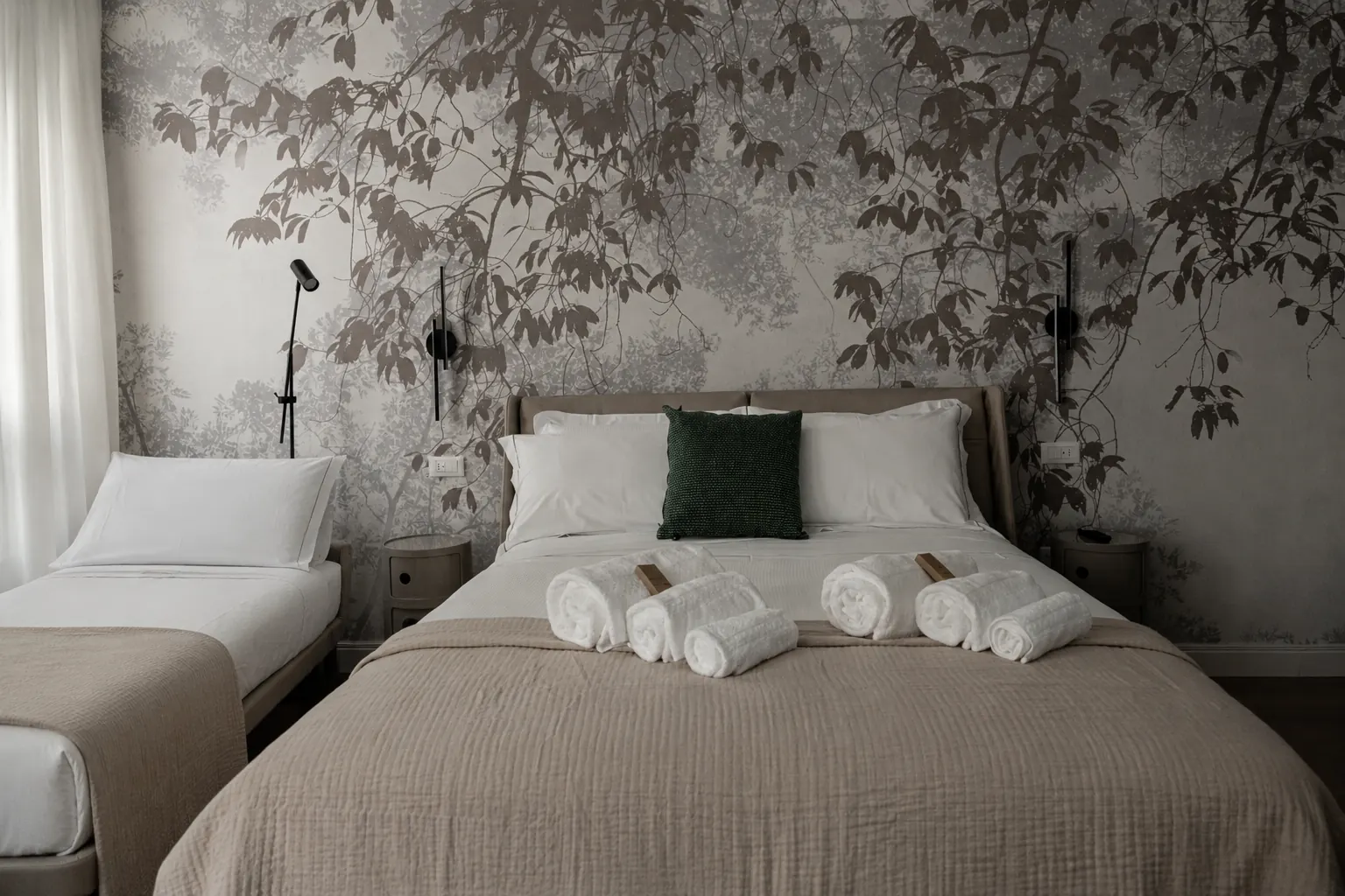 Camera da letto elegante con parete decorativa, letto matrimoniale con cuscini e asciugamani arrotolati, e un letto singolo