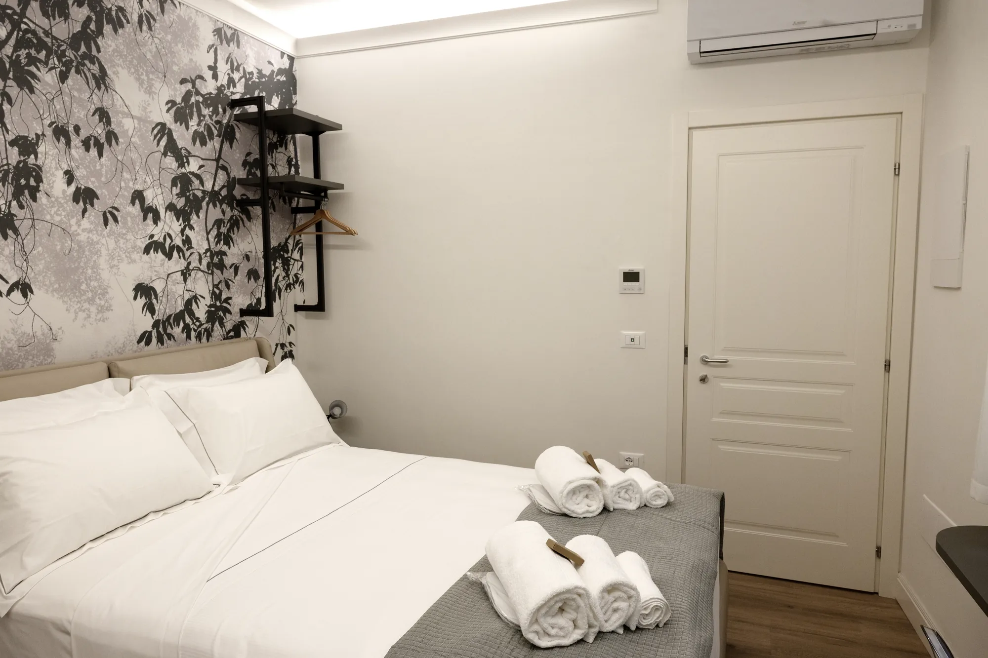 Camera da letto con letto rifatto, asciugamani arrotolati e parete decorata con motivo di foglie