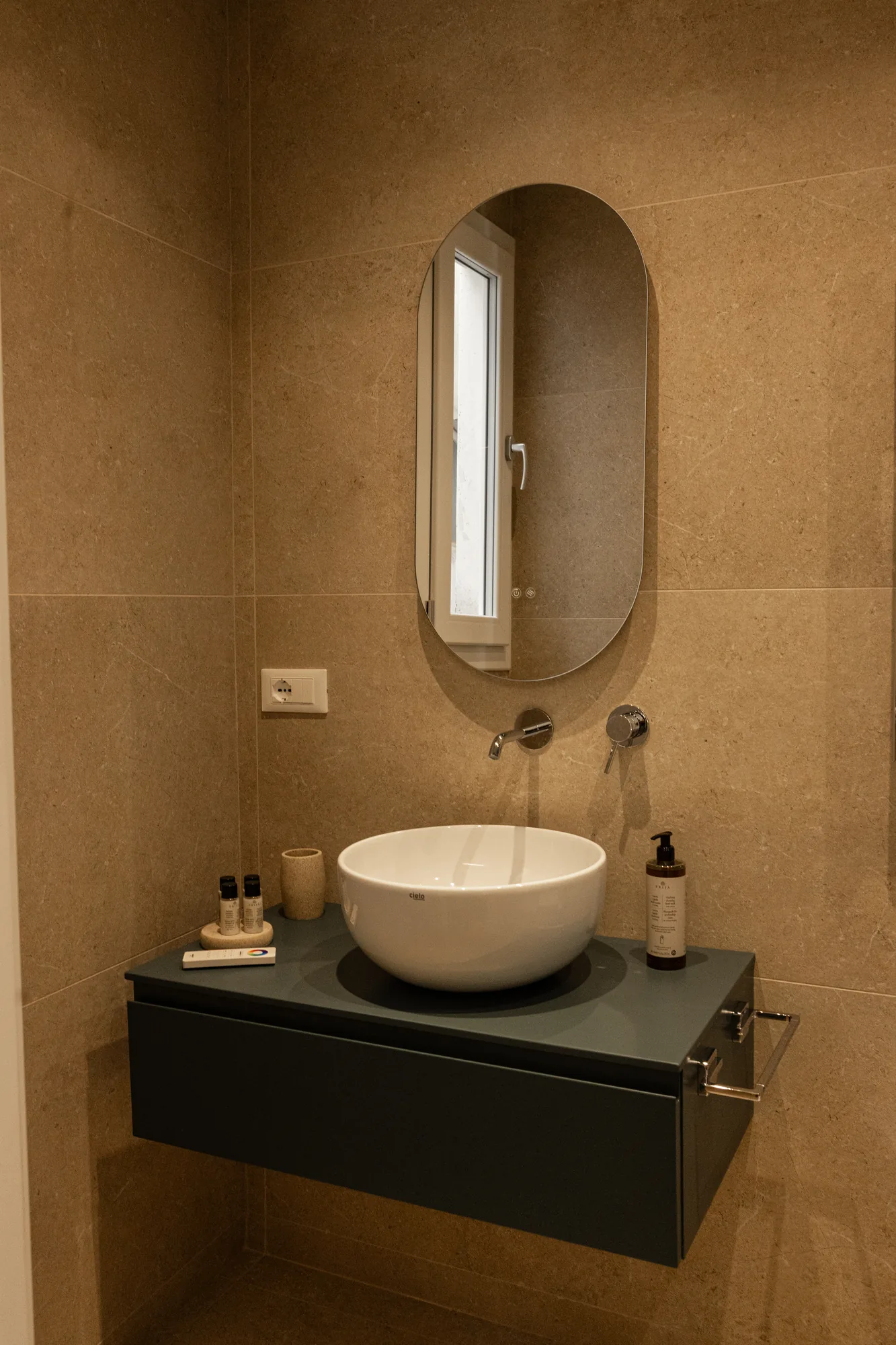 Lavabo da bagno moderno con specchio ovale e pareti rivestite in pietra beige