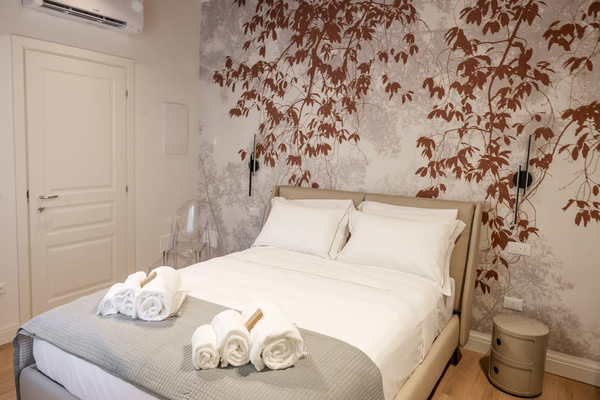 Elegant bedroom with a double bed, rolled towels, and a wall decorated with a leaf pattern
