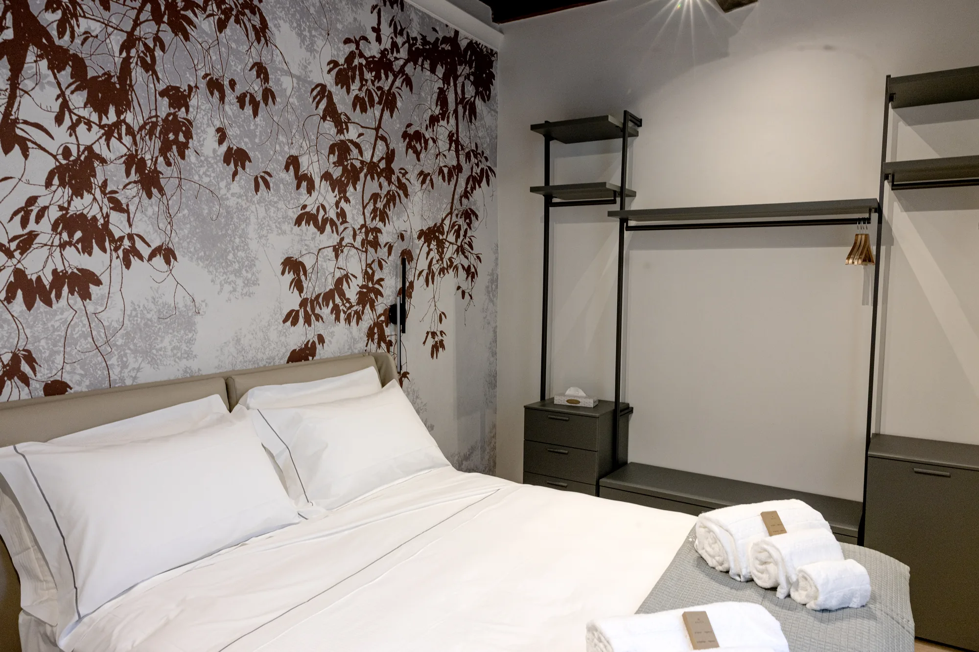 Bedroom with double bed, wall decorated with leaves, and open wardrobe with shelves