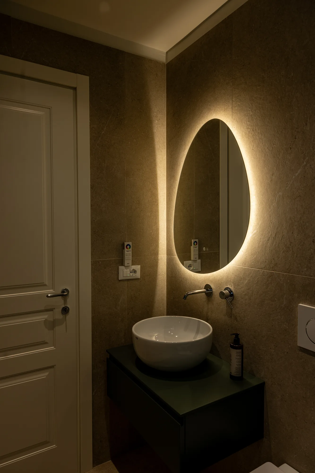 Modern bathroom with countertop sink, backlit mirror, and door on the left