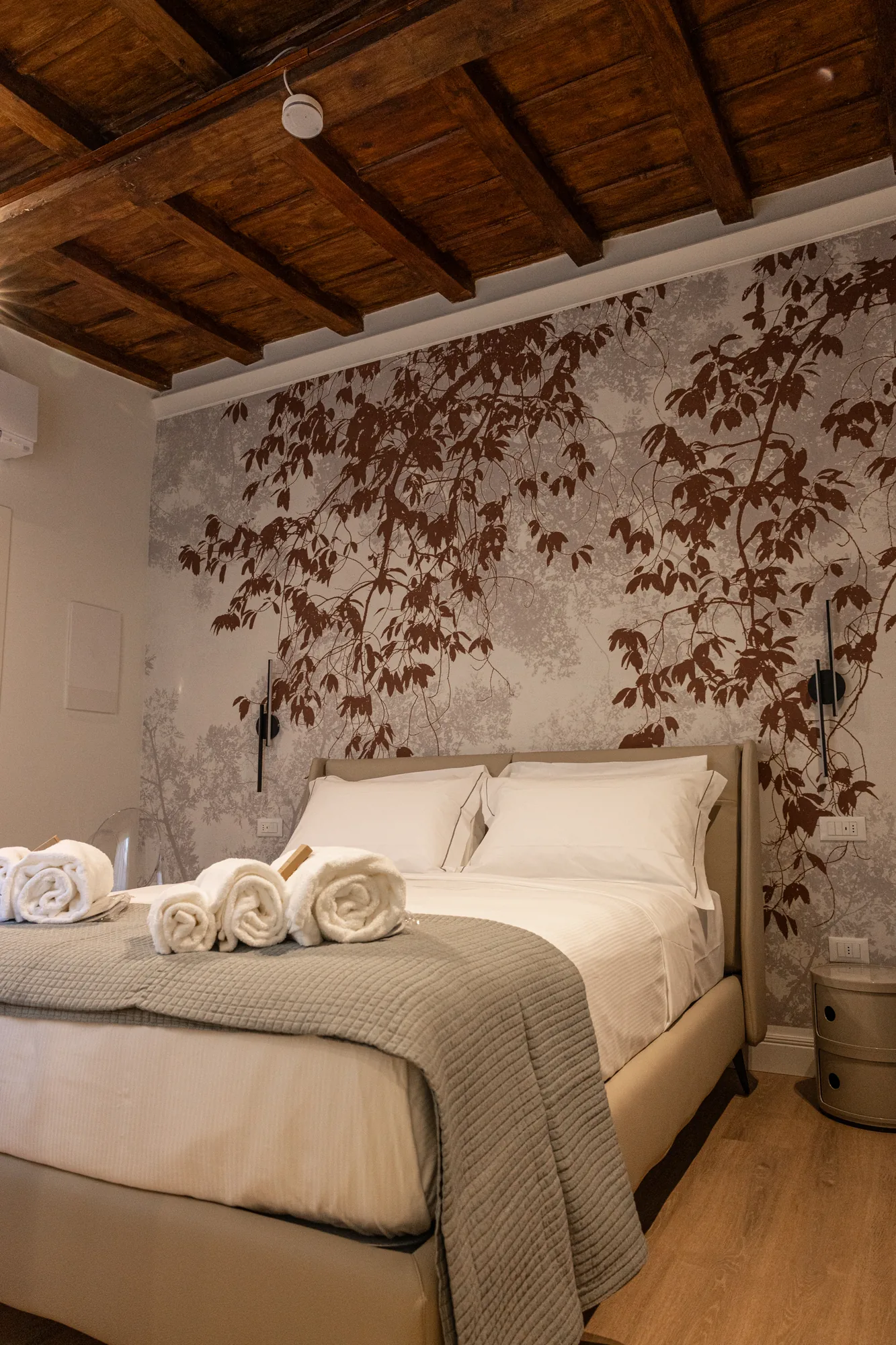 Elegant bedroom with double bed, rolled towels, and wall decorated with a branch pattern