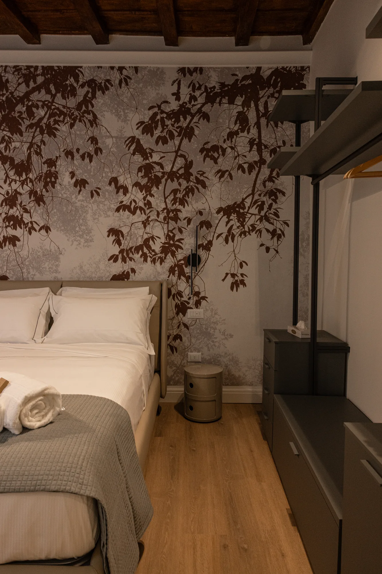 Bedroom with double bed, wallpaper with branches, and dark visible wardrobe