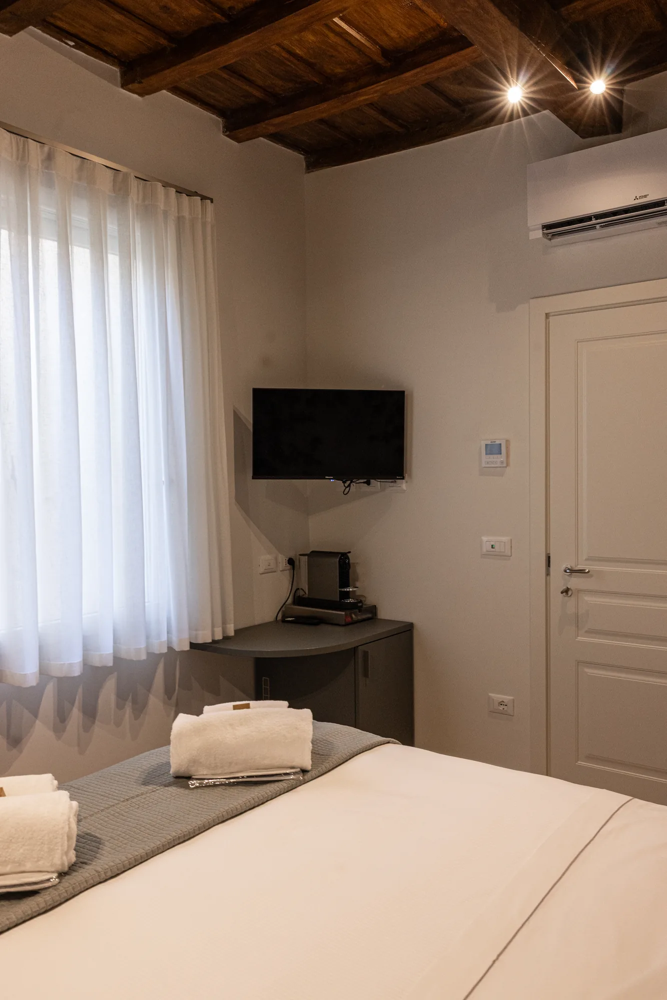 Bedroom with double bed, wall-mounted TV, window with curtains, and ceiling with wooden beams