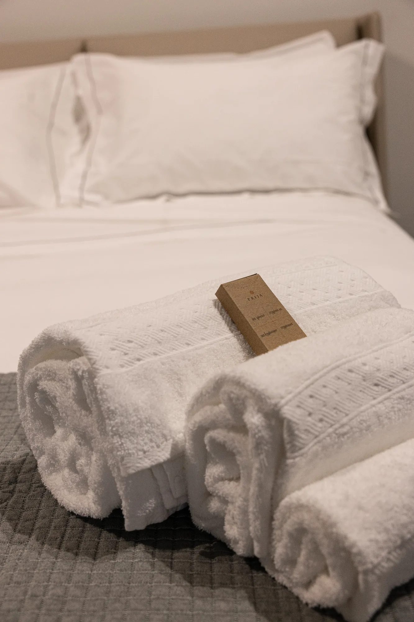 Rolled white towels on a bed with a small bottle of product on top