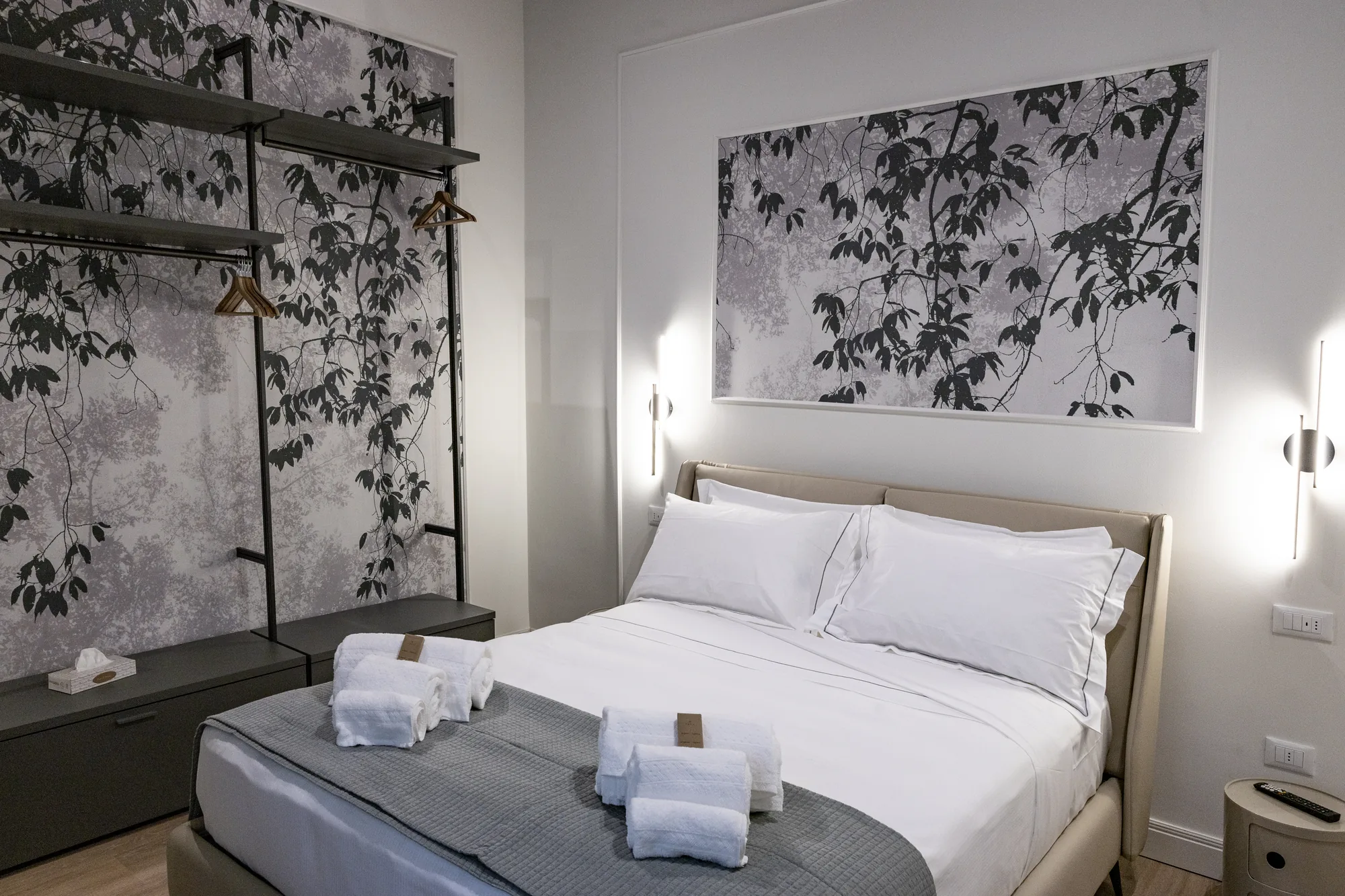 Modern bedroom with made bed, folded towels, and open wardrobe with hangers