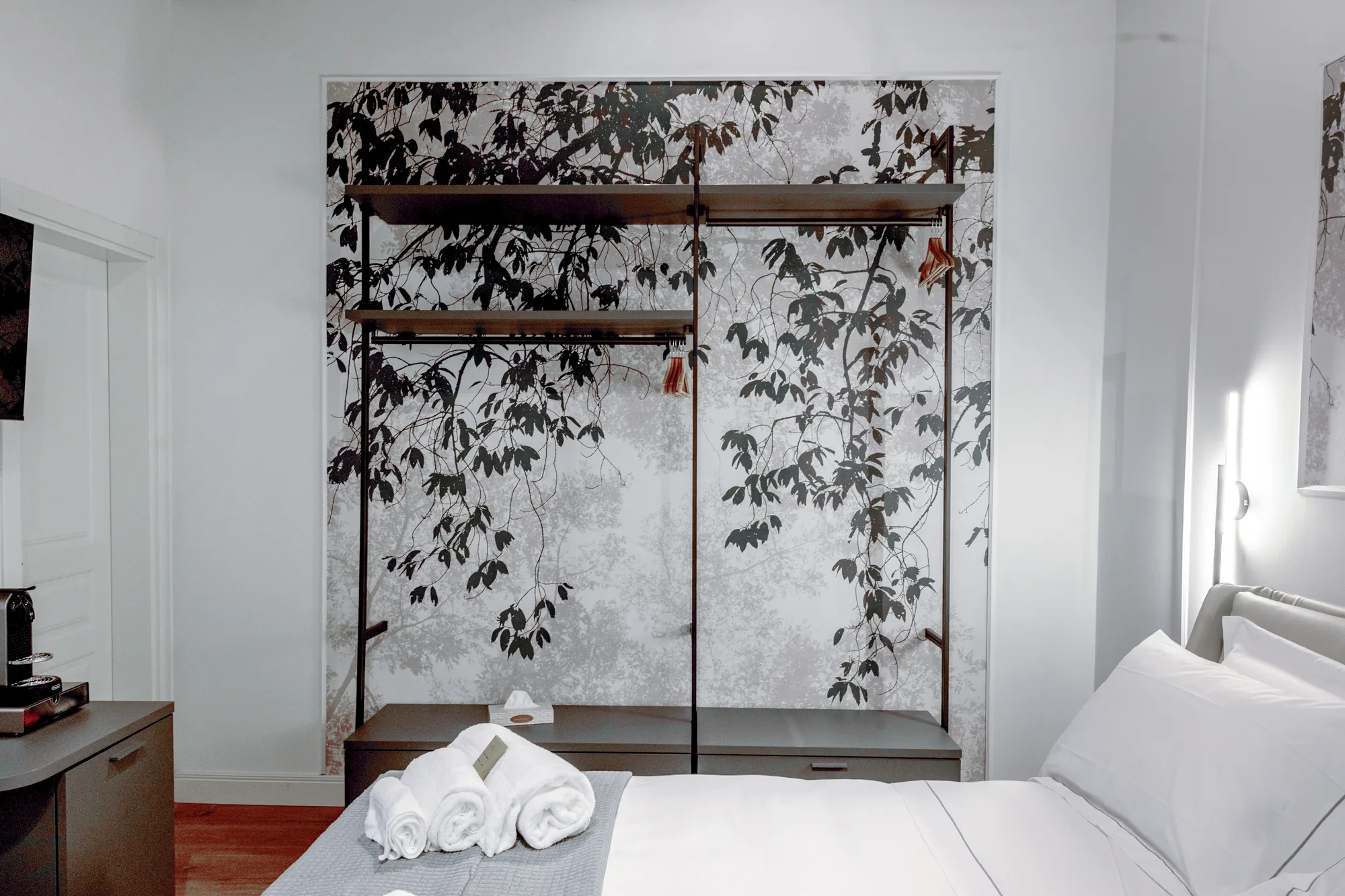Elegant bedroom with a made bed, rolled towels, and an open wardrobe with a decorative leaf background