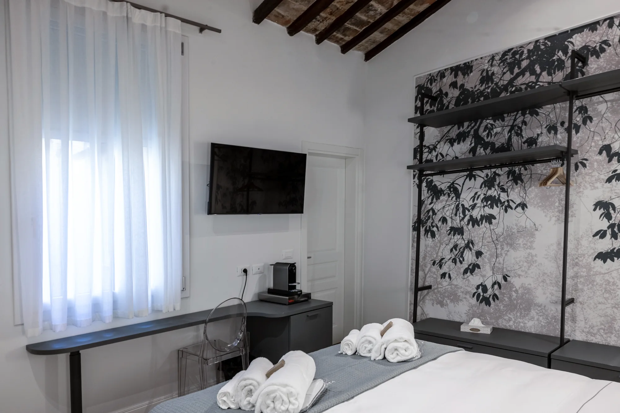Modern bedroom with made bed, folded towels, wall-mounted TV, and open wardrobe