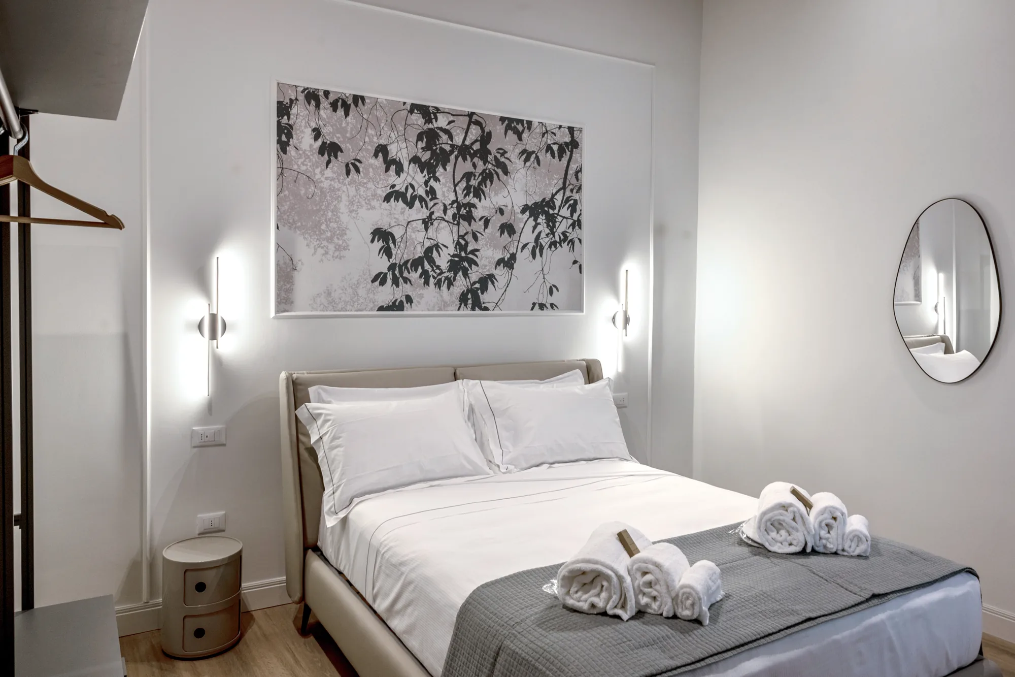 Minimalist bedroom with double bed, folded towels, and oval wall mirror