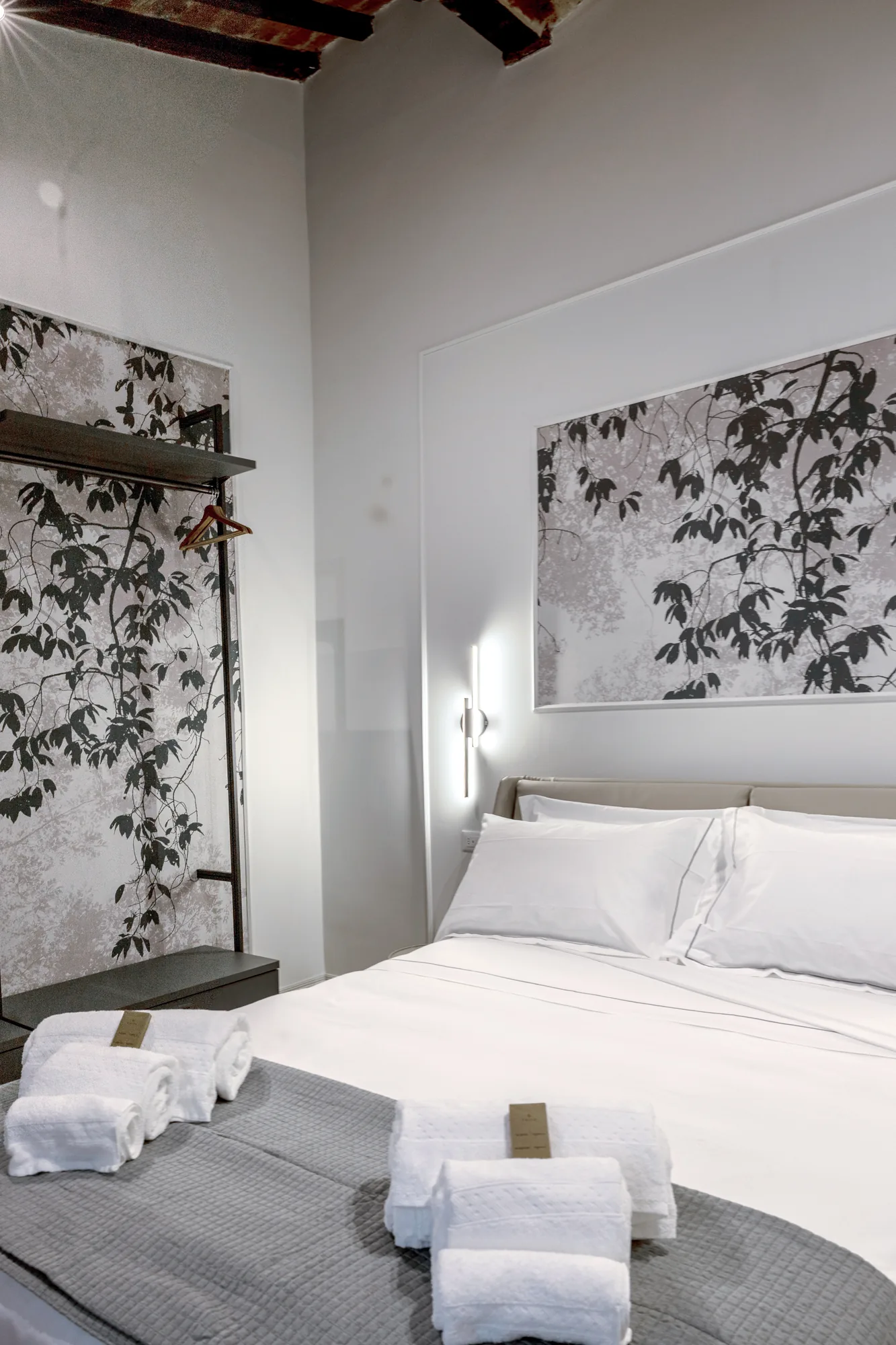 Modern bedroom with made bed, folded towels, and open wardrobe with hangers
