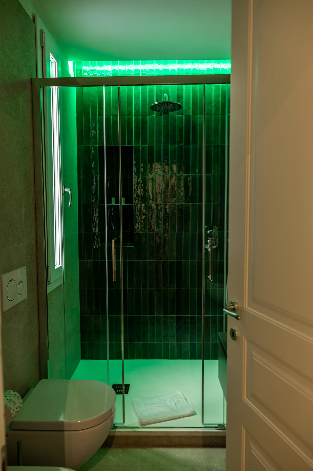 Modern bathroom with green-lit glass shower and toilet in the foreground