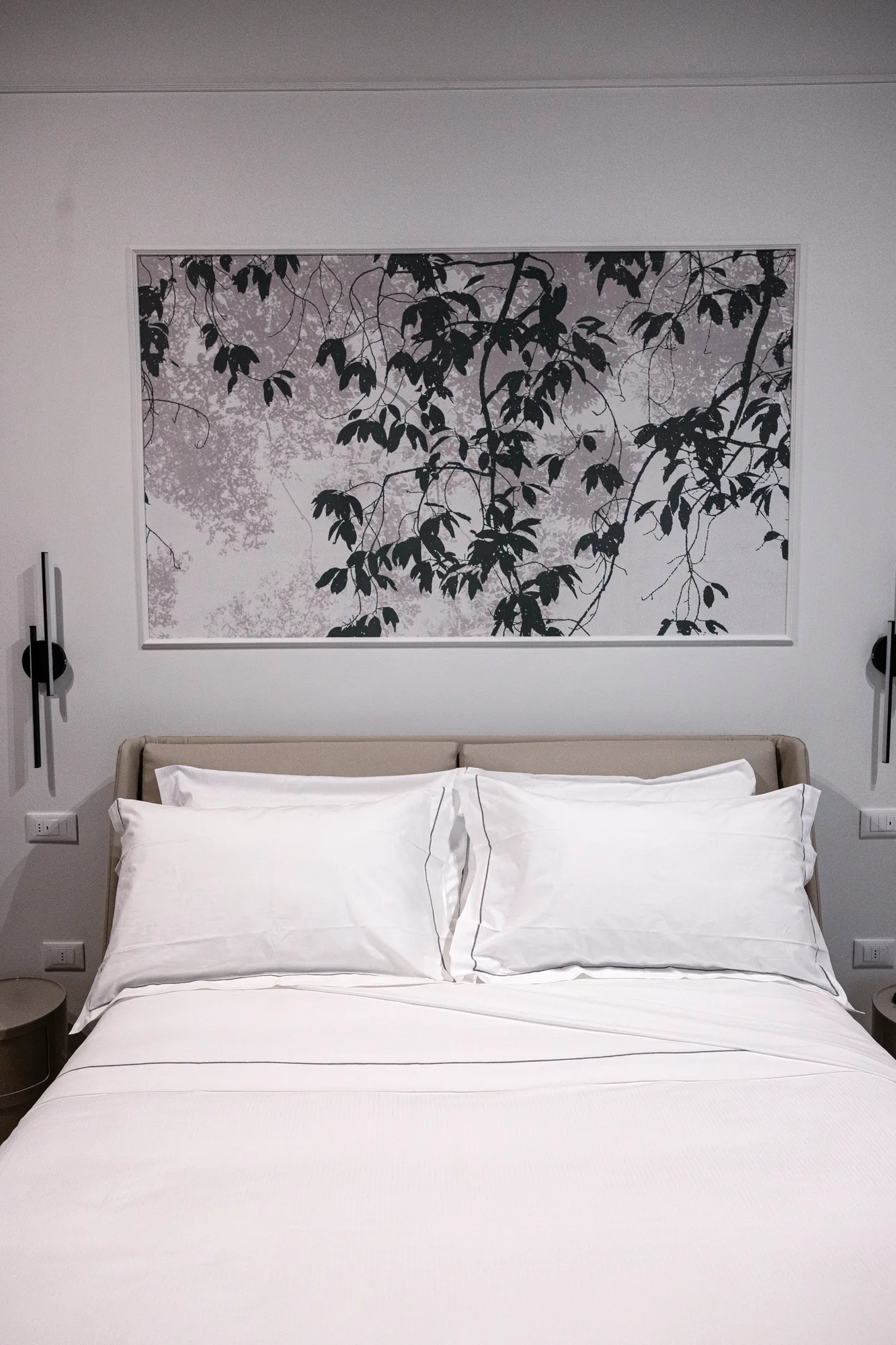 Bedroom with made bed and large black and white botanical painting above the headboard