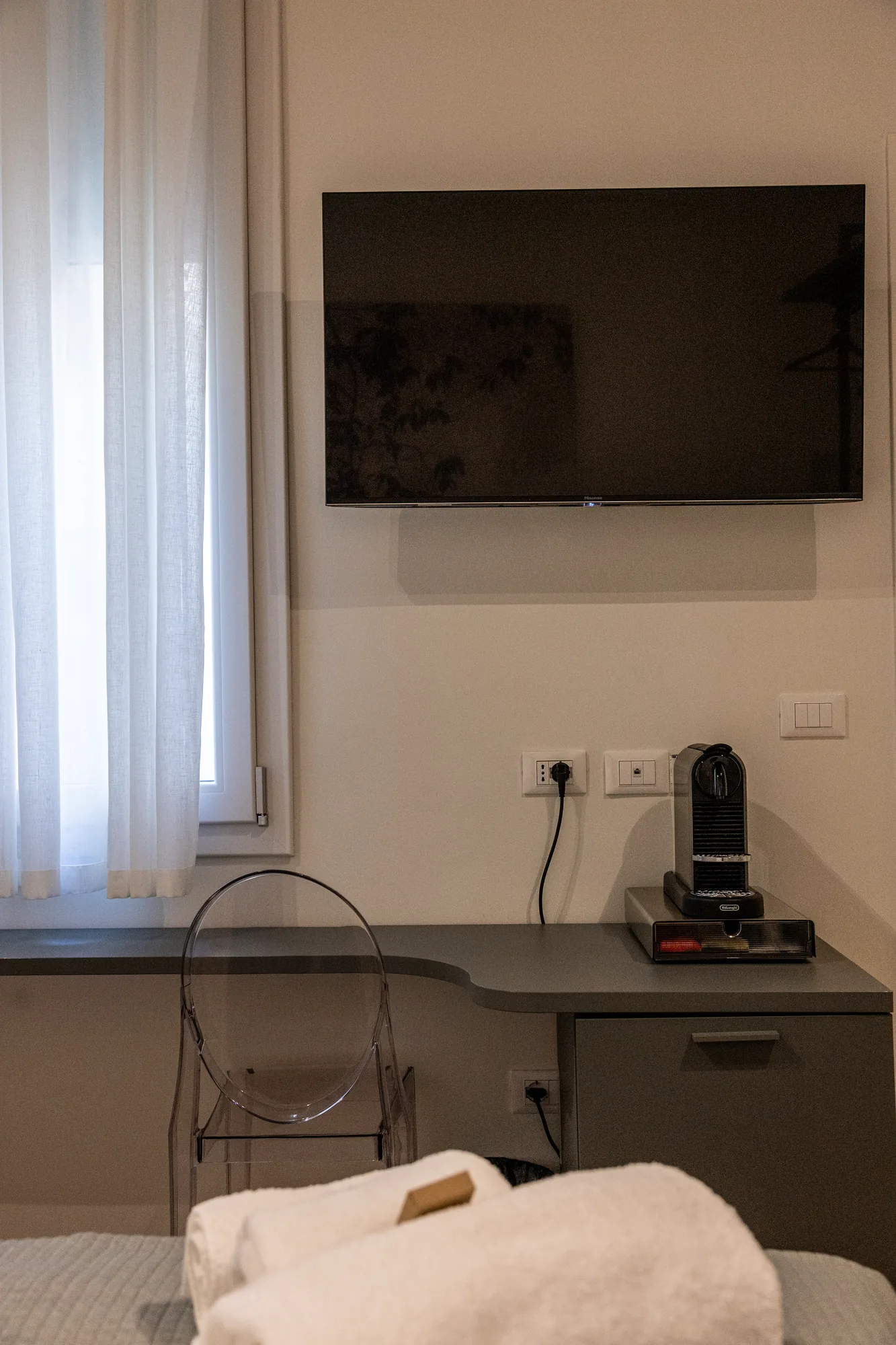 Bedroom with wall-mounted TV, window with curtains, desk, and coffee machine