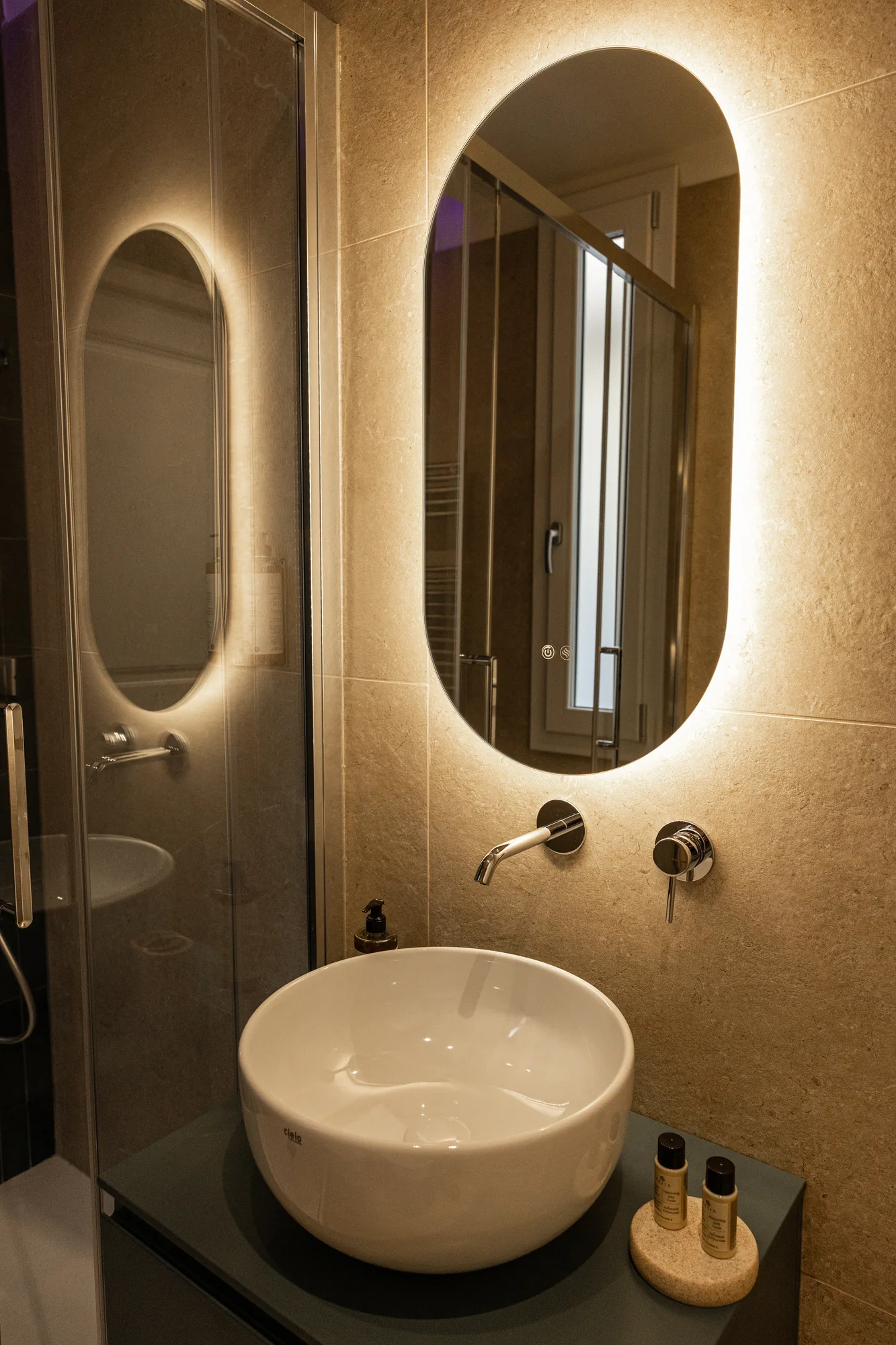 Modern bathroom with countertop sink, backlit mirror, and glass shower