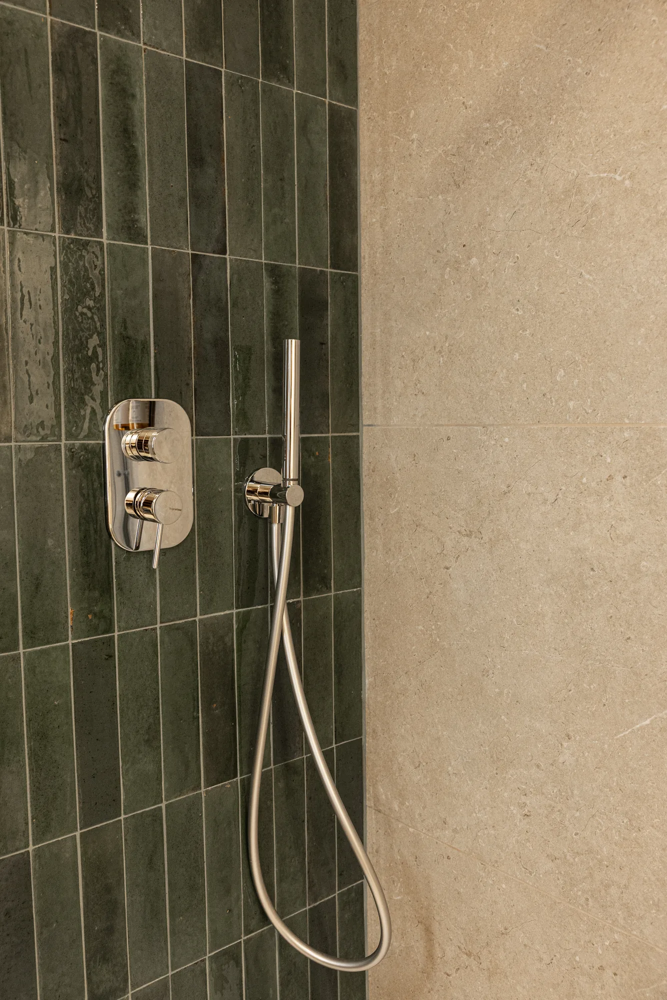 Shower with handheld showerhead and wall controls on green tiled and beige stone covering