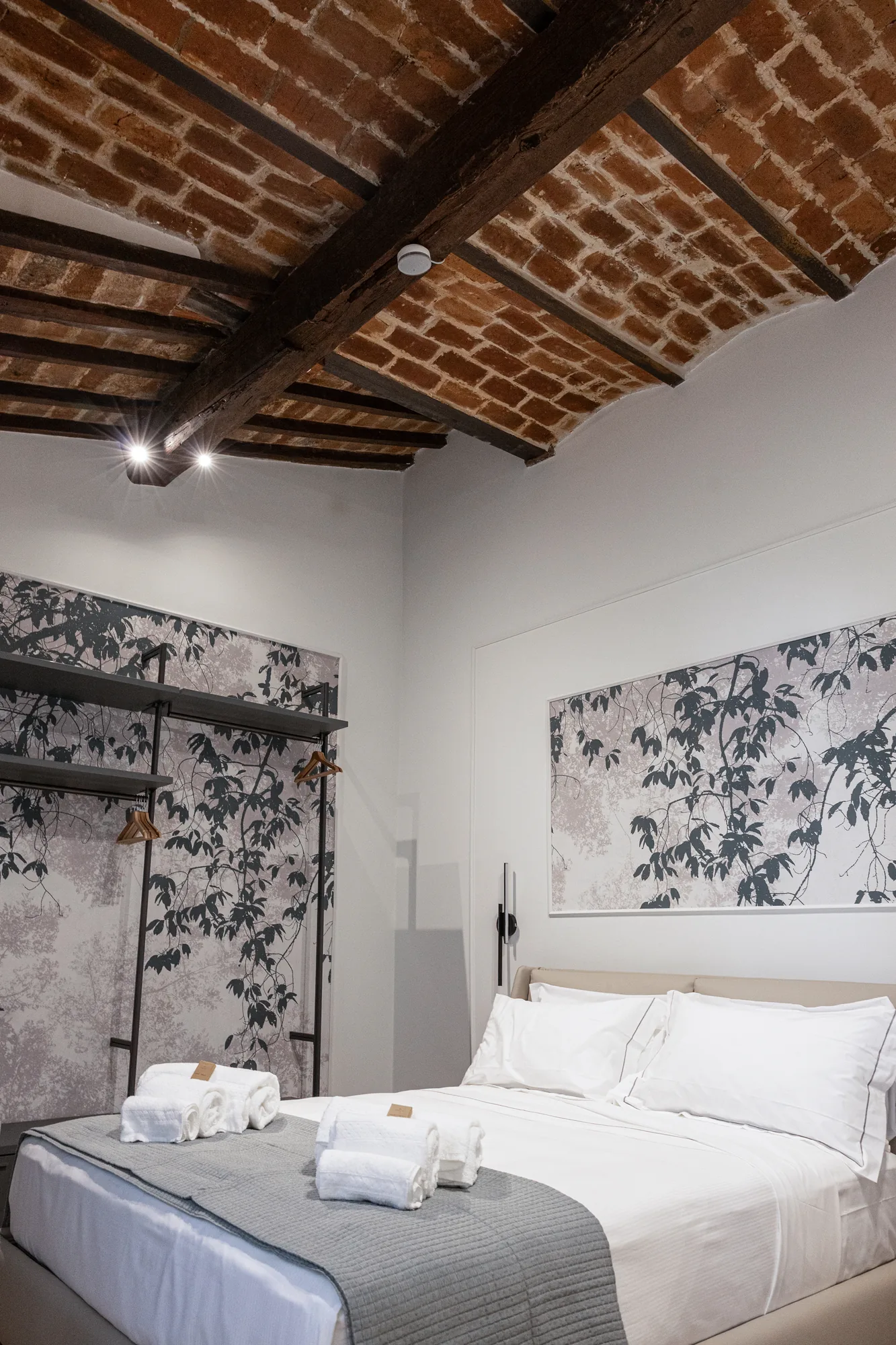 Bedroom with double bed, folded towels, and ceiling with wooden beams and exposed bricks